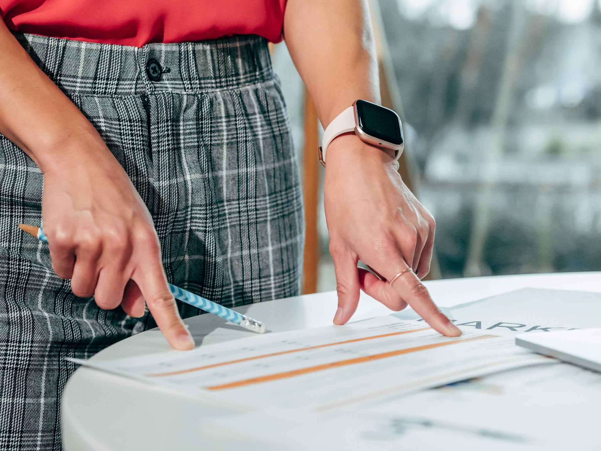 Businesswoman examining documents on a desk with a smartwatch and pen.