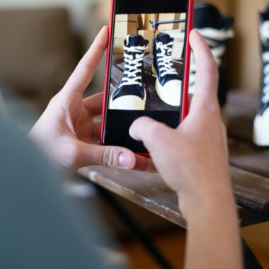 Hands hold smartphone to photograph sneakers indoors, showcasing mobile photography.