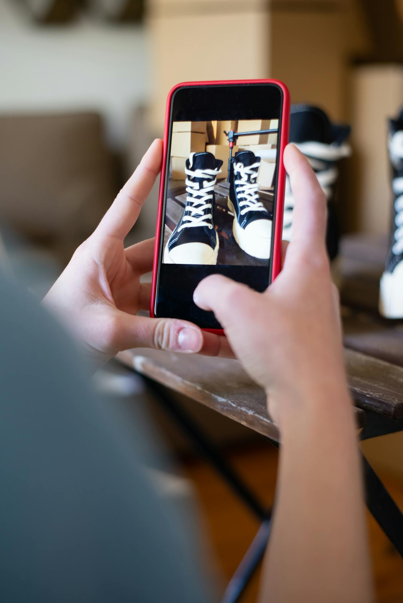 Hands hold smartphone to photograph sneakers indoors, showcasing mobile photography.