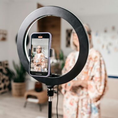 Senior woman creating content at home using smartphone and ring light in a modern setting.