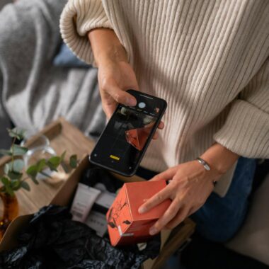 Woman captures product packaging with smartphone, highlighting personal branding.